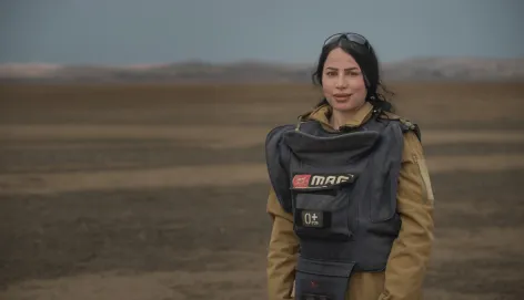 Noora Murad wearing protective gear looks at the camera from a mine field in Iraq.