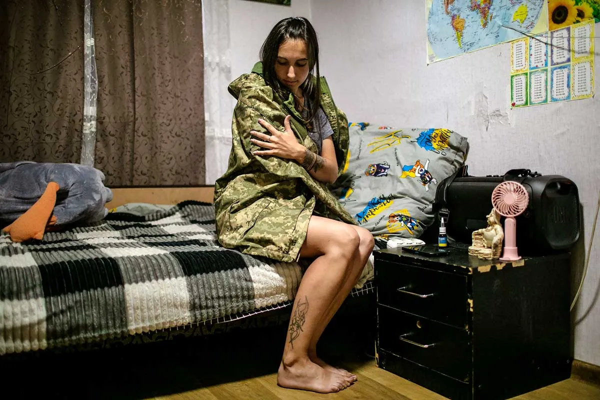Viktoriia Koroliova sits on the edge of a bed and holds her husband's fatigue jacket close